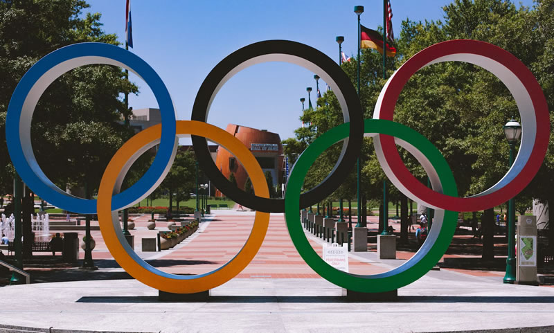 Eine Statue der fünf olympischen Ringe auf einem Platz umgeben von Bäumen
